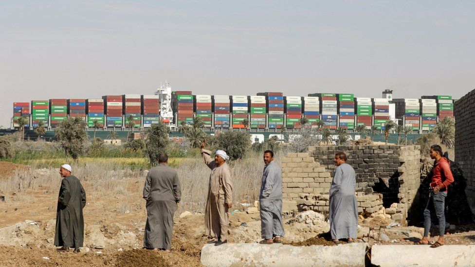 Onlookers watch as a container ship stuck for days in the Suez Canal resumes its travel